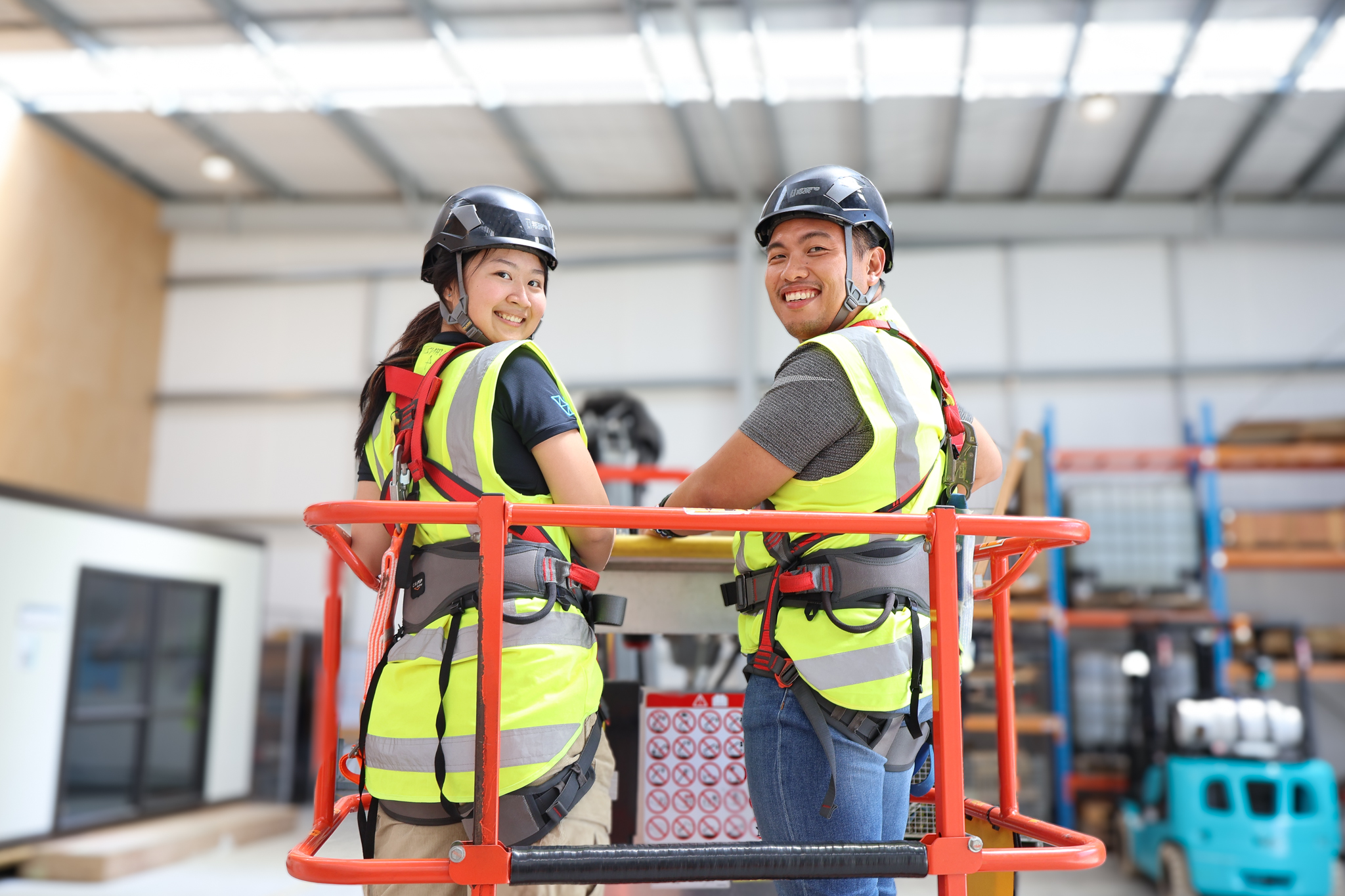 Two construction workers are being trained on how to use the MEWP. They are standing in the bucket of a boom lift.