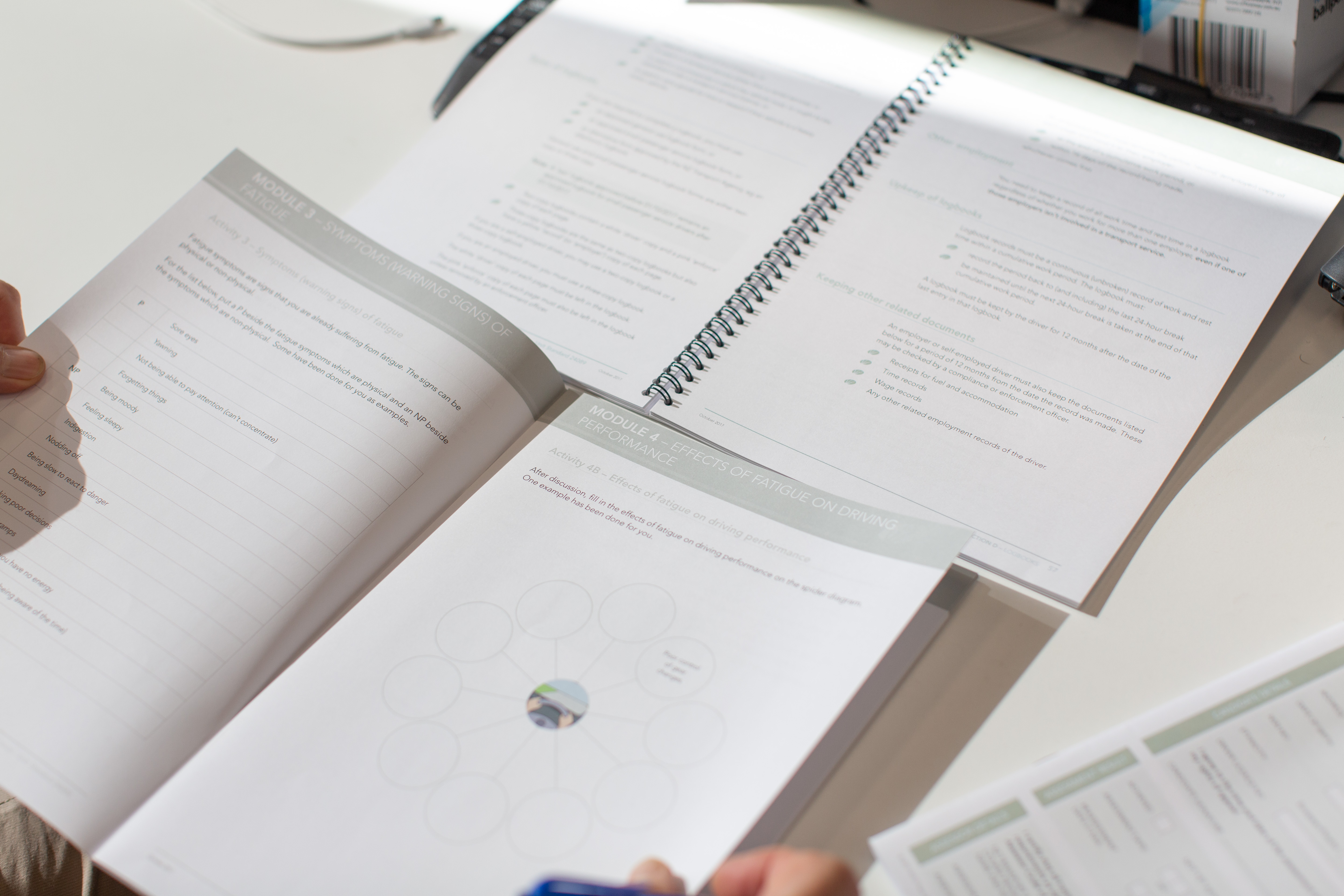 A learner is reading a training manual on a desk. 